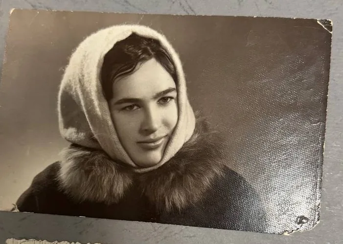 A worn portrait still in its album, photographed with a phone — corners bumped, surface dulled by glare